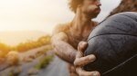 Fit muscular man performing lateral exercises using a medicine ball during sunrise on an empty road for his med ball training exercises