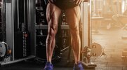 Man standing in front of a piece of leg exercising gym equipment showing his muscular legs after performing a Lower Body Strength Training Program