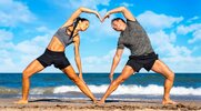 Fit young couple practicing yoga poses on the beach in a heart shape pose