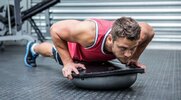 Muscular fit man performing a bosu ball workouts with a bosu ball pushup exercise