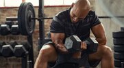 Bald fitness enthusiast working out with a single dumbbell increasing his training intensity with a full-body dumbbell workout