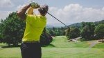 Golfer wearing a titleist hat swinging a hybrid golf club from the tee box with perfect from to avoid golfing injuries.