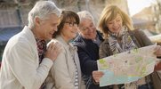 A group of aging people looking at a city map as the travel outdoors in a new foreign city