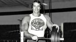 Young Arnold Schwarzenegger standing behind a barbell bench after working out