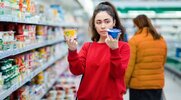 Young female shopper comparing two different yogurts in the dairy aisle of a grocery store