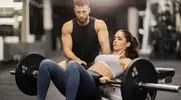 Male fitness trainer teaching his client how to perform a hip thruster correctly