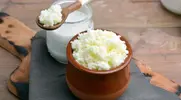 Kefir with probiotics on a wooden spoon and clay bowl next to a cup of milk