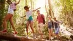 Group of friends crossing a river on a tree log in the forest while social distancing