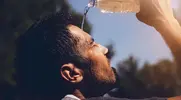 Young fit man suffering from exertion headaches splashing water on his face during a heatwave