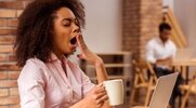 Young black female with afternoon brain fog yawning with a cup a coffee in her hand