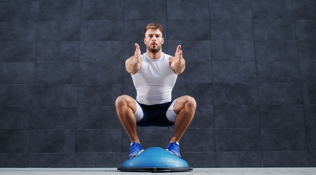 Fit Muscular man performing a squat on a bosu ball training exercises